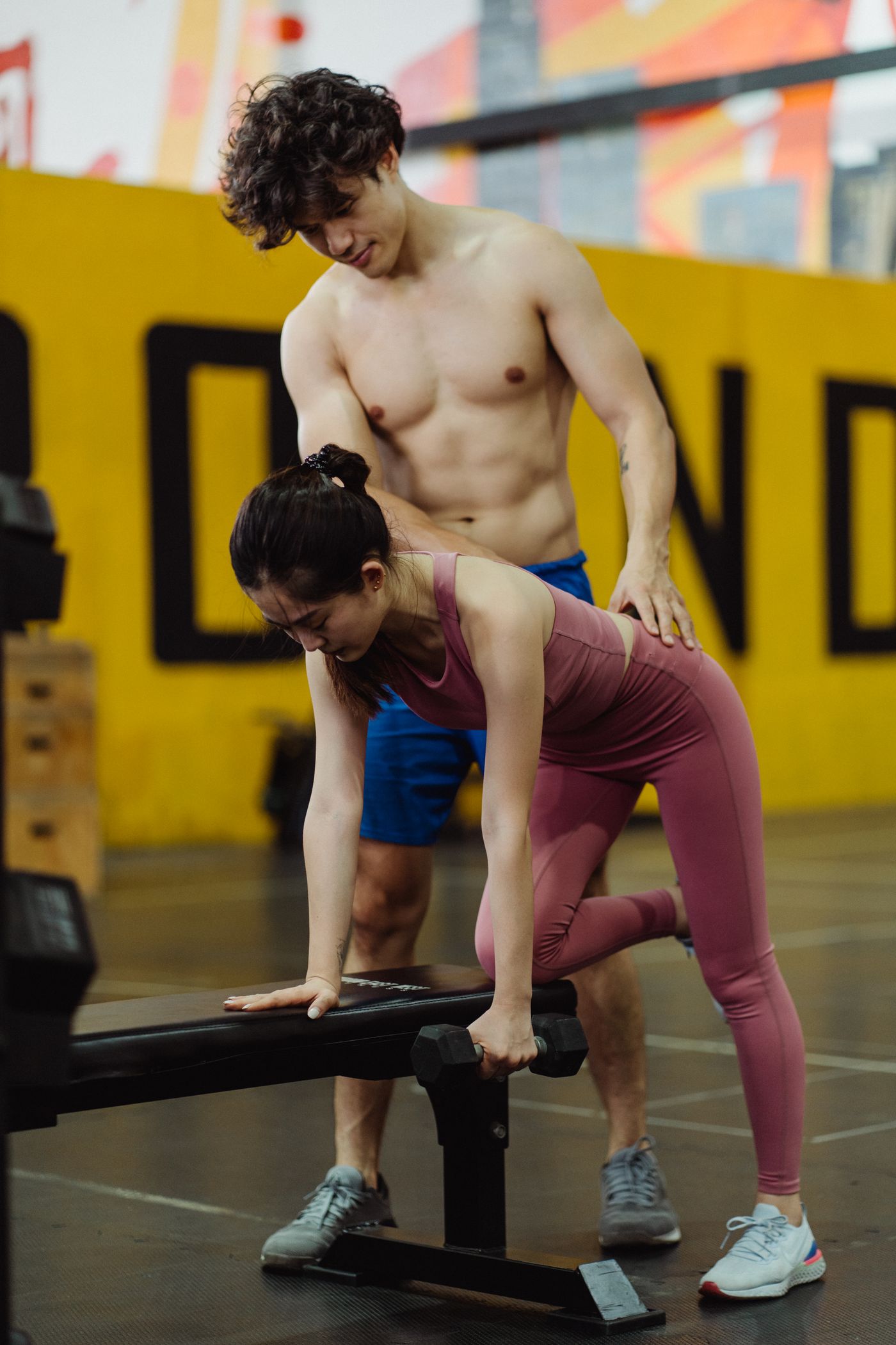 A person performing a dumbbell row with a trainer